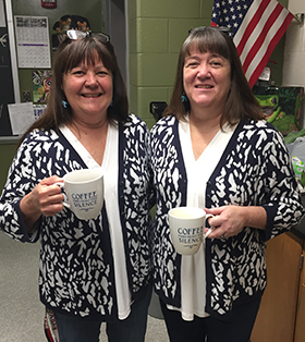two teachers in matching sweaters holding coffee mugs